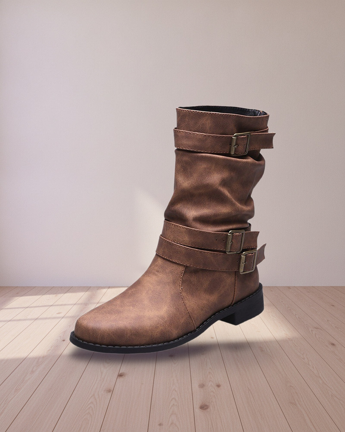 Brown buckled mid-calf boot, side view on a wood floor